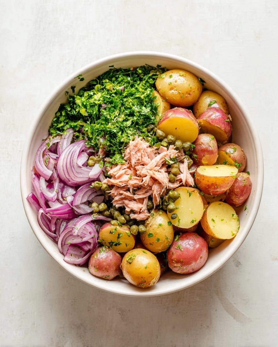 A white bowl set on a white marbled surface holds a layered potato salad. The bottom layer is made up of halved small potatoes in both red and yellow skins, creating a mix of reddish and soft yellow colors with a smooth texture. On top of the potatoes, there is a sprinkling of green capers scattered in small clusters. Shredded pinkish tuna flakes are placed in the center. Bright green chopped fresh parsley covers one section. Thin slices of crisp purple-red onions fill another section, their translucent layers curling slightly. The ingredients are arranged mostly side by side without mixing, showing clear separation of colors and textures. photo taken with an iphone --ar 4:5 --v 7