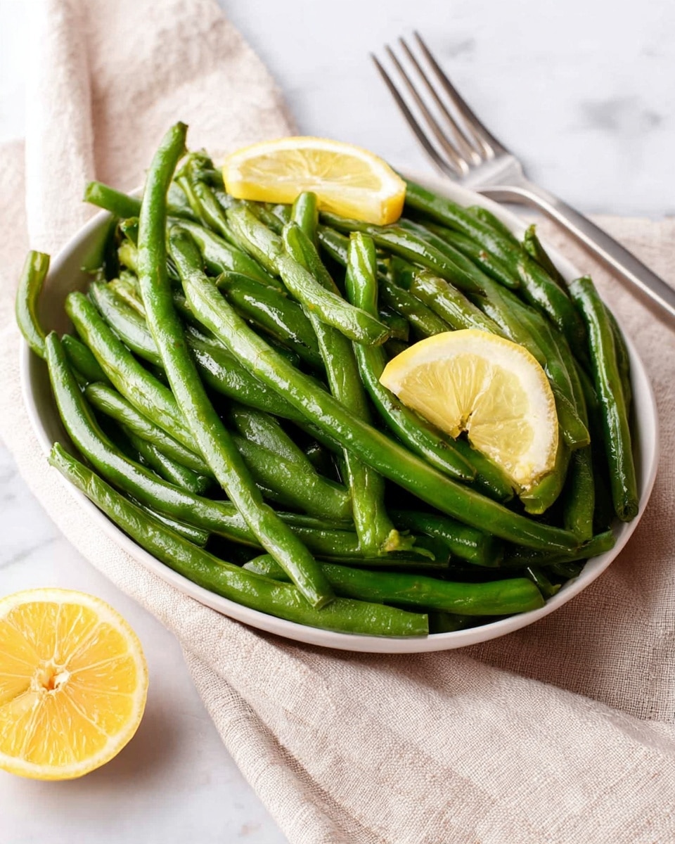 A baking tray filled with a single layer of cooked green beans scattered across the surface. The green beans are a mix of bright and slightly darker green shades with a light oily shine and some small black pepper specks visible on their skin. The tray has a worn metal texture, and it sits on a white marbled surface. photo taken with an iphone --ar 4:5 --v 7
