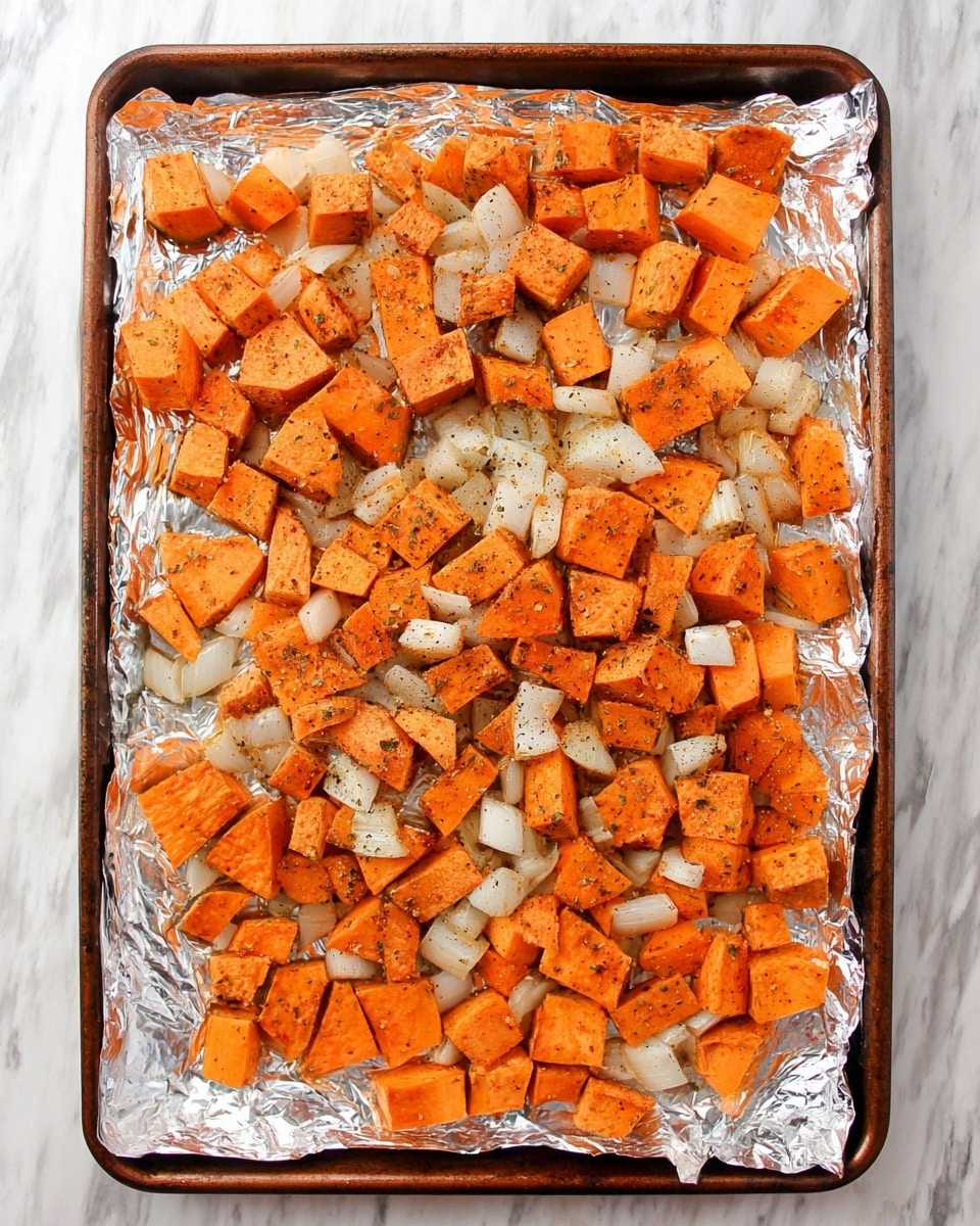 The image shows a baking tray lined with shiny aluminum foil filled with evenly spread cubed sweet potatoes and diced white onions. The sweet potatoes are bright orange with a slightly glossy texture from seasoning, while the onions are translucent with light browning. Both vegetables are coated with visible flecks of black pepper and green herbs, creating a seasoned, rustic look. The tray sits on a white marbled surface, and the ingredients cover the entire tray without overlapping too much. photo taken with an iphone --ar 4:5 --v 7