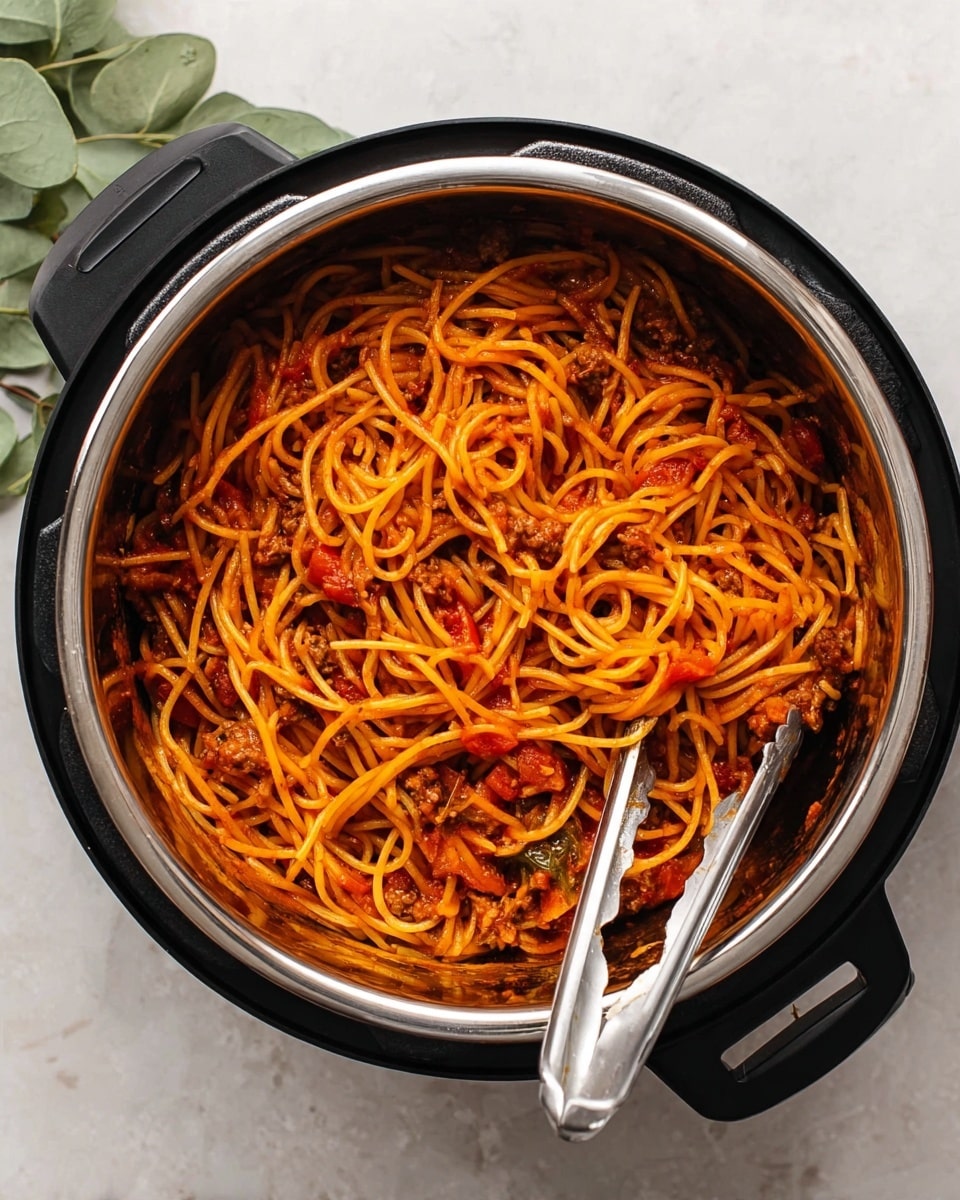 A close-up top view of a black electric pot with a silver inner pot filled with cooked spaghetti mixed in rich red tomato sauce with small pieces of cooked meat and visible chunks of tomato. A pair of metal tongs rests inside the pot, partly submerged in the spaghetti, showing the long, thin noodles coated evenly with the sauce. The pot is placed on a white marbled surface with a green plant leaf partially visible in the top left corner. photo taken with an iphone --ar 4:5 --v 7
