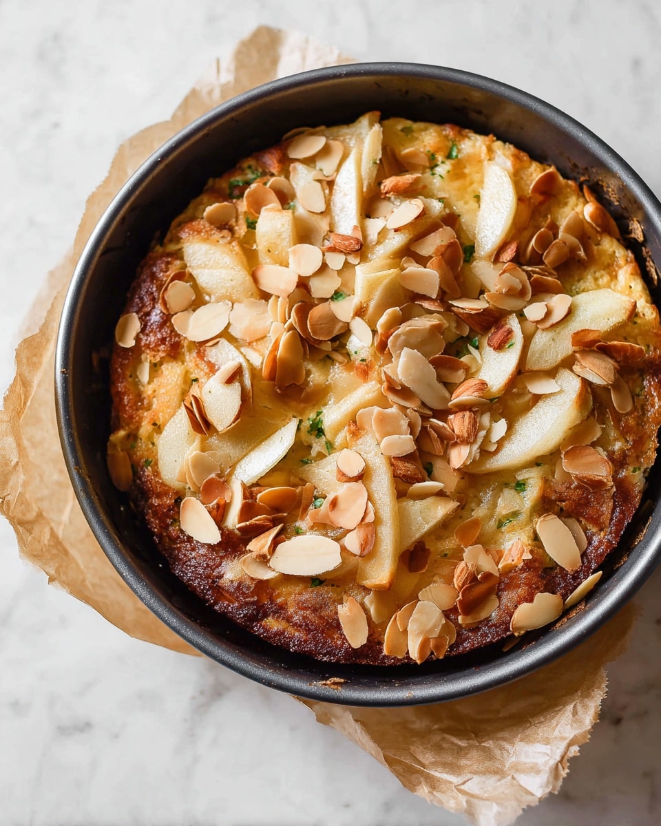 A round, baked dessert sits inside a black pan with a slightly raised edge. The top layer is golden brown and uneven, covered with thin, overlapping slices of light-colored fruit, possibly apple, and scattered toasted almond flakes that add texture and a mix of tan and light brown hues. The edges and some parts of the surface have deeper brown caramelized spots, giving a slightly crisp look. The pan rests on a piece of crumpled brown parchment paper placed on a white marbled surface. photo taken with an iphone --ar 4:5 --v 7