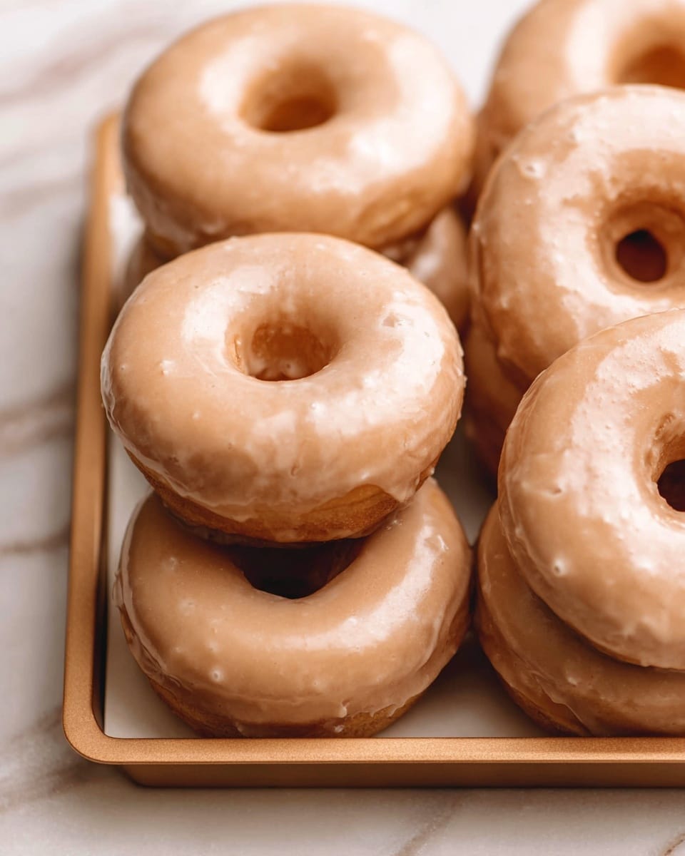 A close-up shot of seven round donuts stacked and resting on a light brown baking tray placed on a white marbled surface, each donut topped with a smooth, light brown glaze that covers the entire top and drips slightly down the sides, giving a glossy texture with small air bubbles and soft highlights, the donuts have a soft golden-brown base visible through the hole at the center, arranged with one donut prominently in the front and the others grouped closely behind, photo taken with an iphone --ar 4:5 --v 7