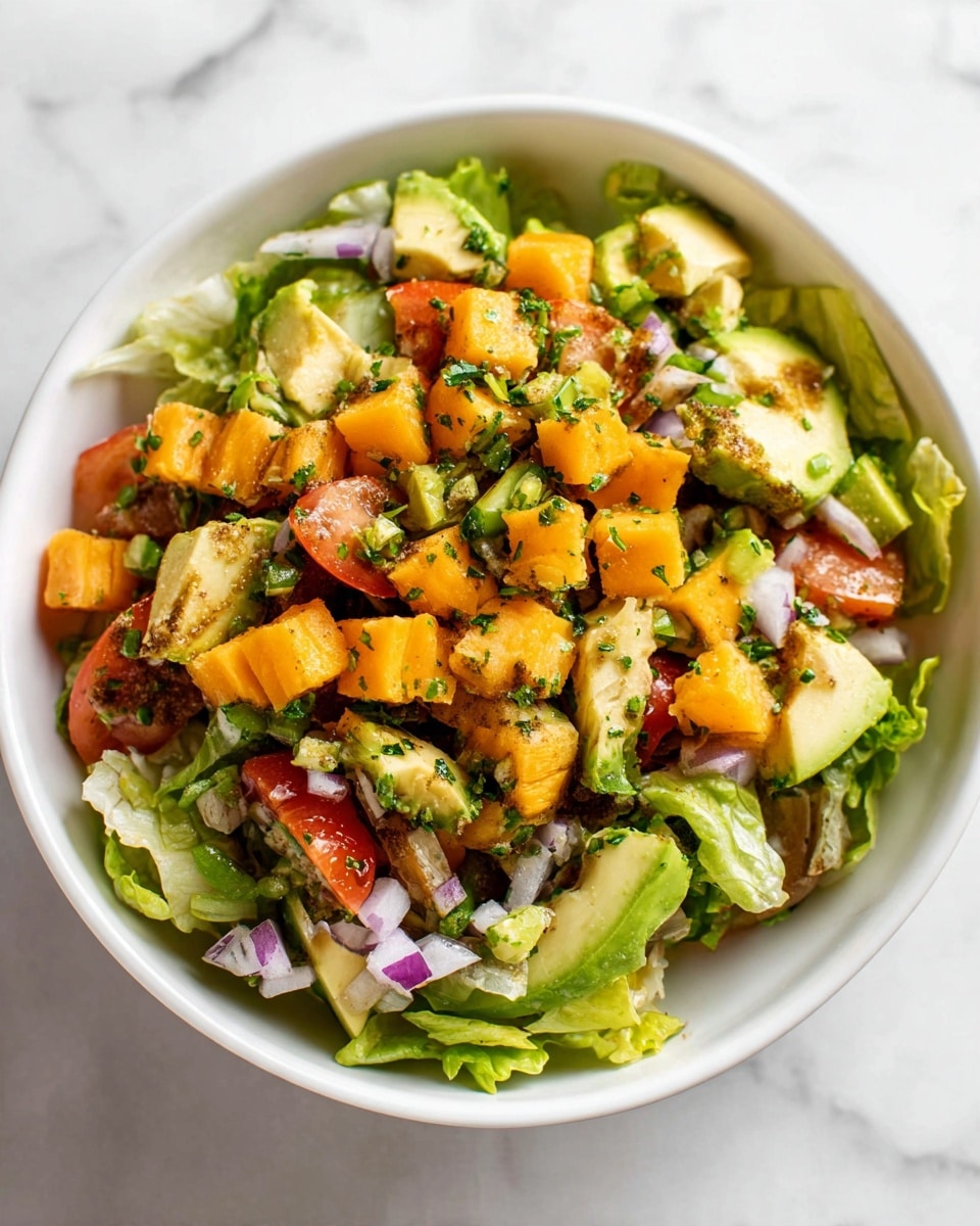 A white bowl filled with a fresh salad sits on a white marbled surface. The salad has a bottom layer of green leafy lettuce, roughly torn. On top, there are small cubes of bright orange cheese, diced red tomatoes, chopped green avocado, thin slices of green pickles, and small pieces of purple onion, all mixed evenly across the bowl. The colors are bright and fresh, contrasting well with the white bowl and marbled background. Photo taken with an iphone --ar 4:5 --v 7