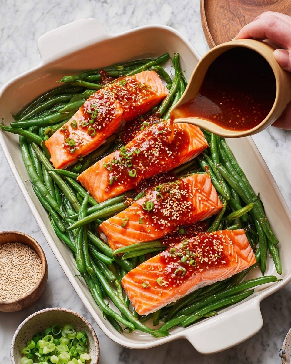 A white baking dish holds three raw salmon fillets placed on a layer of fresh green beans. The salmon is bright orange with white marbling lines and is topped with a reddish-brown sauce sprinkled with sesame seeds. The green beans underneath are long and green, some of them also lightly coated with the sauce. A woman’s hand is pouring more sauce over the salmon and green beans from a beige cup. Around the dish, there are small bowls holding white sesame seeds and chopped green onions. The whole scene is set on a white marbled surface. photo taken with an iphone --ar 4:5 --v 7