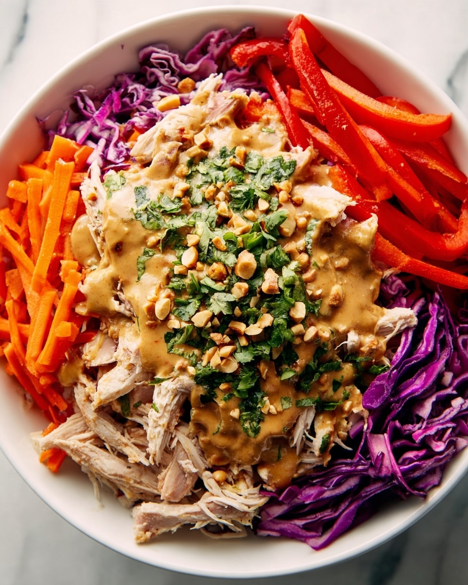 A white bowl holds a colorful layered dish starting with shredded cooked chicken at the bottom covered with a creamy, light brown sauce. On top of the chicken, there is a layer of chopped fresh green herbs mixed with crushed nuts, adding texture. Surrounding this center, the bowl is filled with thin orange carrot sticks, bright red bell pepper strips, and deep purple cabbage shreds, all fresh and raw. The sauce slightly drizzled over the vegetables adds a glossy finish. The bowl is placed on a white marbled surface. photo taken with an iphone --ar 4:5 --v 7